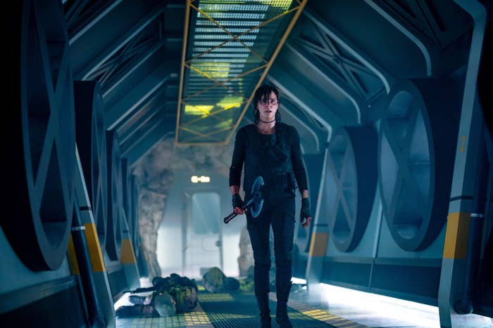Person in futuristic corridor holding weapon, dressed in tactical gear. Sci-fi setting with industrial design