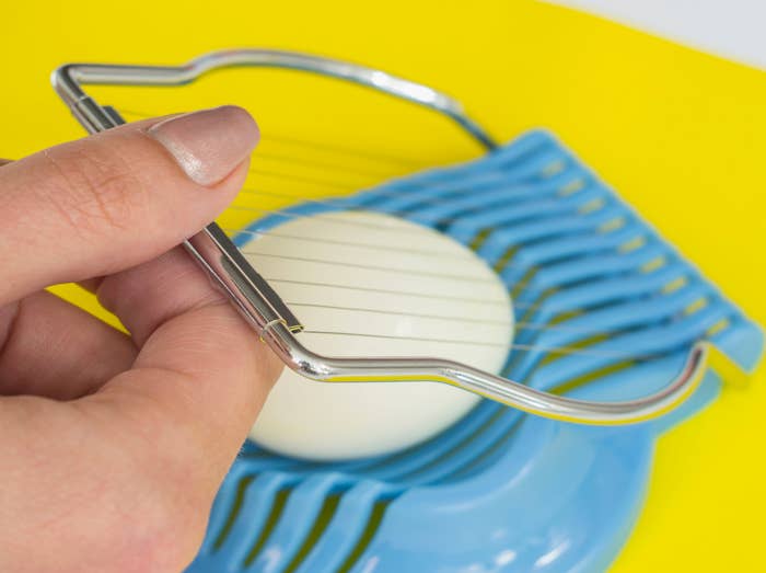 Hand slicing a boiled ovum  connected  a ligament  ovum  slicer with a yellowish  background