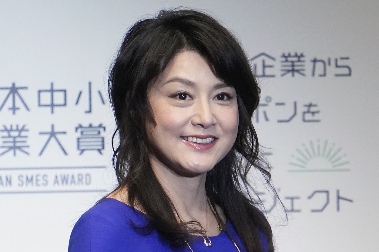 すみませんが、この画像の人物が誰かわかりません。ただし、青いドレスを着た女性が笑顔でポーズをとっています。バックグラウンドにテキストがあります。