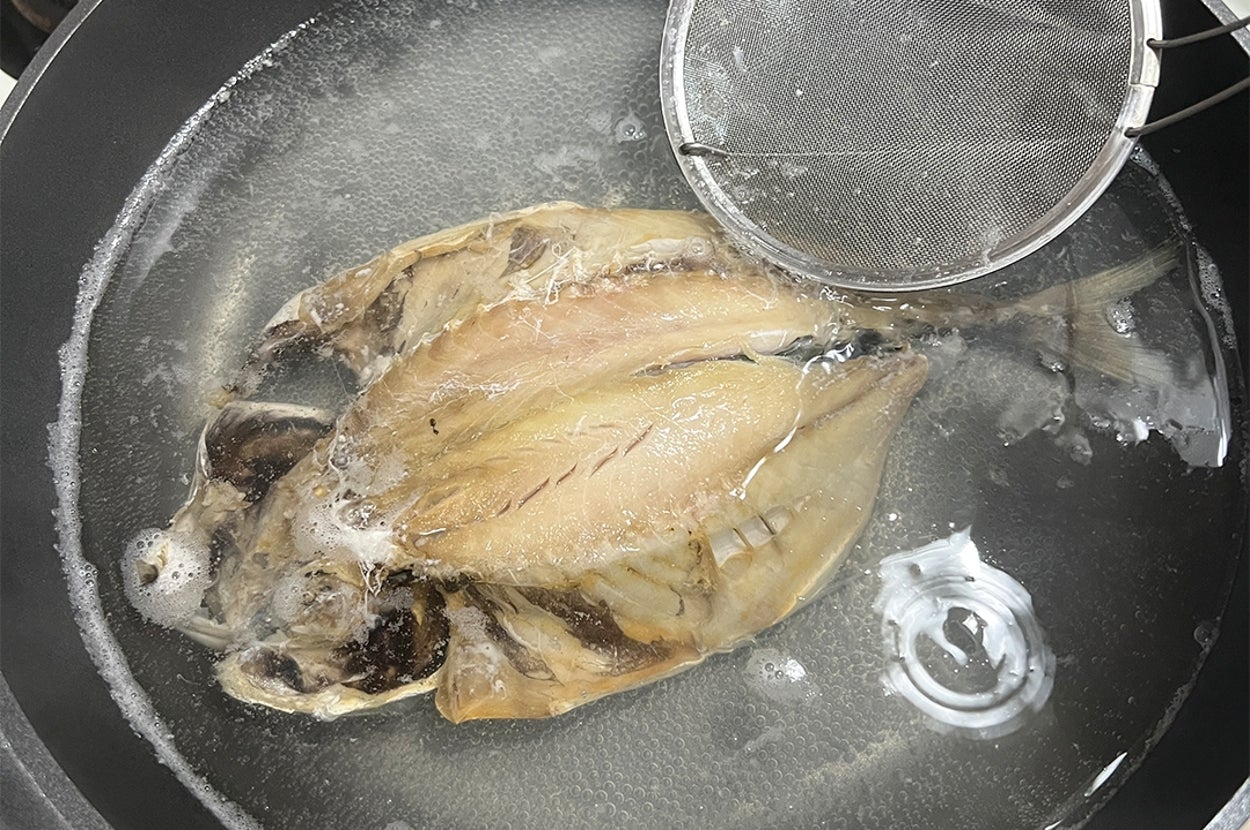 鍋で魚を煮込み中。脇に泡を除くためのシメが入っている。