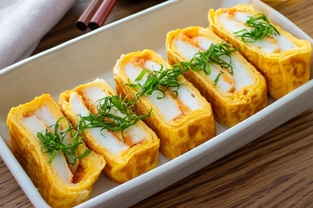 卵で巻かれたかまぼこのスライスが皿に並び、上に刻んだ薬味がのせられている。食卓にはお茶も見えます。