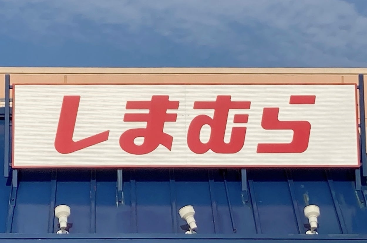 Storefront with a sign displaying Japanese text, "しまむら," likely indicating a name or brand. Blue awning with a wheelchair accessibility sign