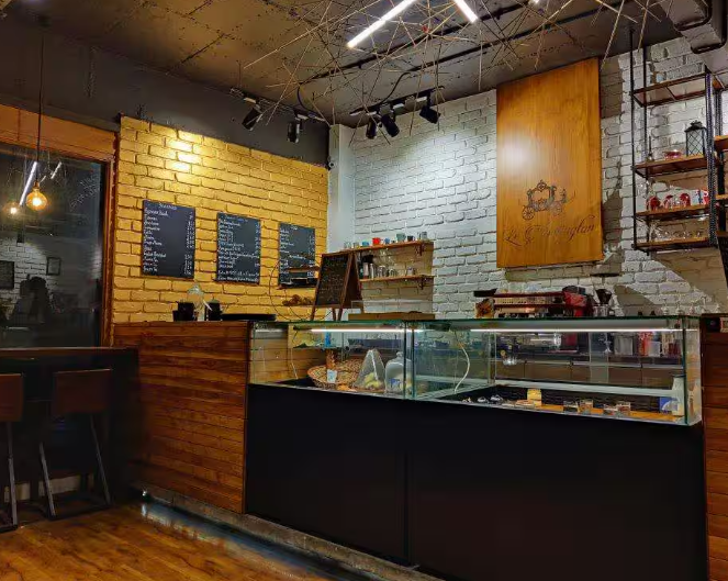 Cozy café interior with a glass display counter, menu boards on a brick wall, and a warm ambiance