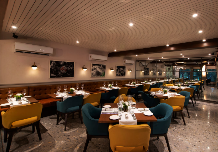 Upscale restaurant interior with neatly set tables, cushioned chairs, and ambient lighting. Framed art decorates the walls