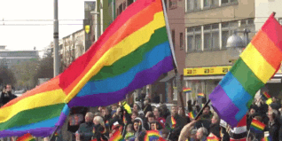 A crowd of people marching, waving large rainbow flags during a pride parade
