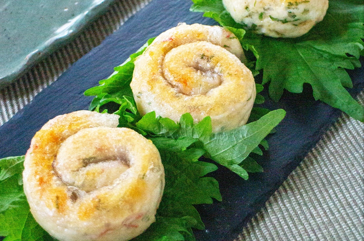 3つの生葉にのった焼き餃子が黒い皿に並んでいる。奥にタレが置かれている。