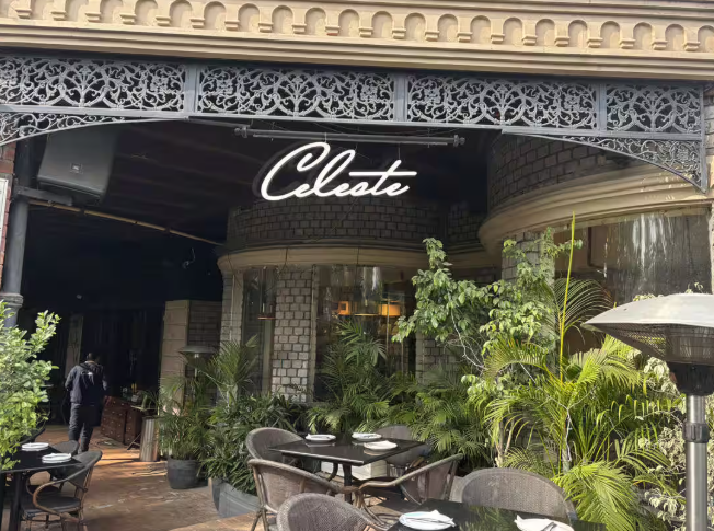 Entrance of a restaurant named &quot;Celeste&quot; with outdoor seating and lush greenery
