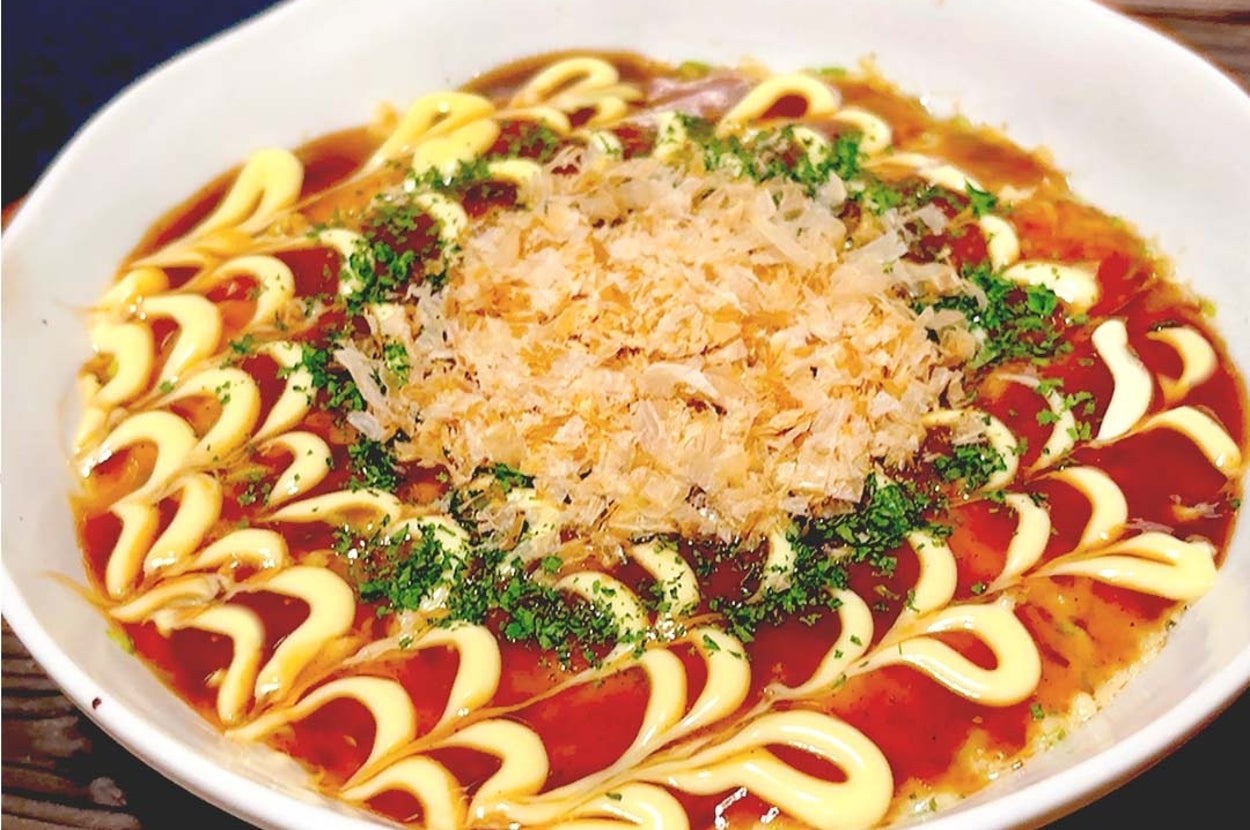日本の鉄板焼き料理、お好み焼きが皿に盛られている。ソースとマヨネーズが波状にかけられ、鰹節と青のりがトッピングされている。