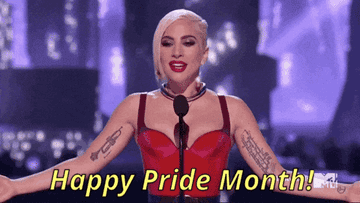 Person in a stylish outfit stands on stage, arms open, with &quot;Happy Pride Month!&quot; text displayed