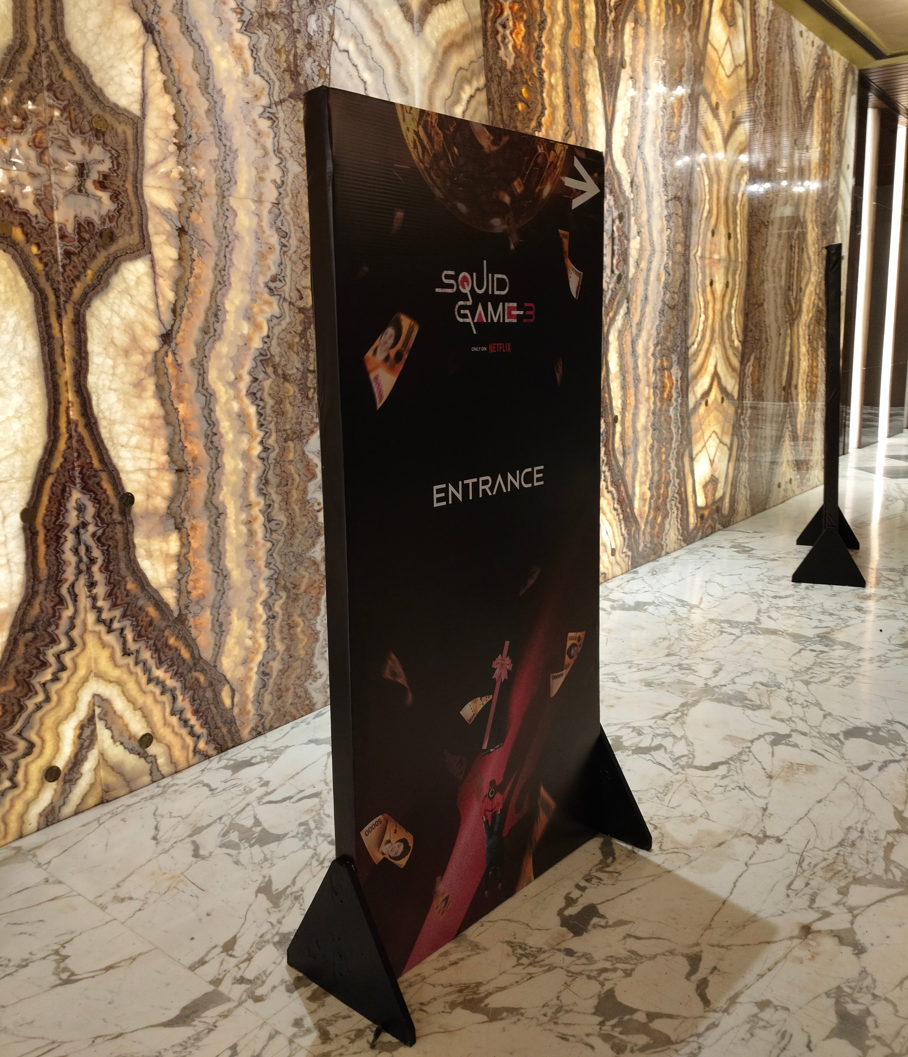 Sign for "Squid Game" event entrance in a marble-floored hallway