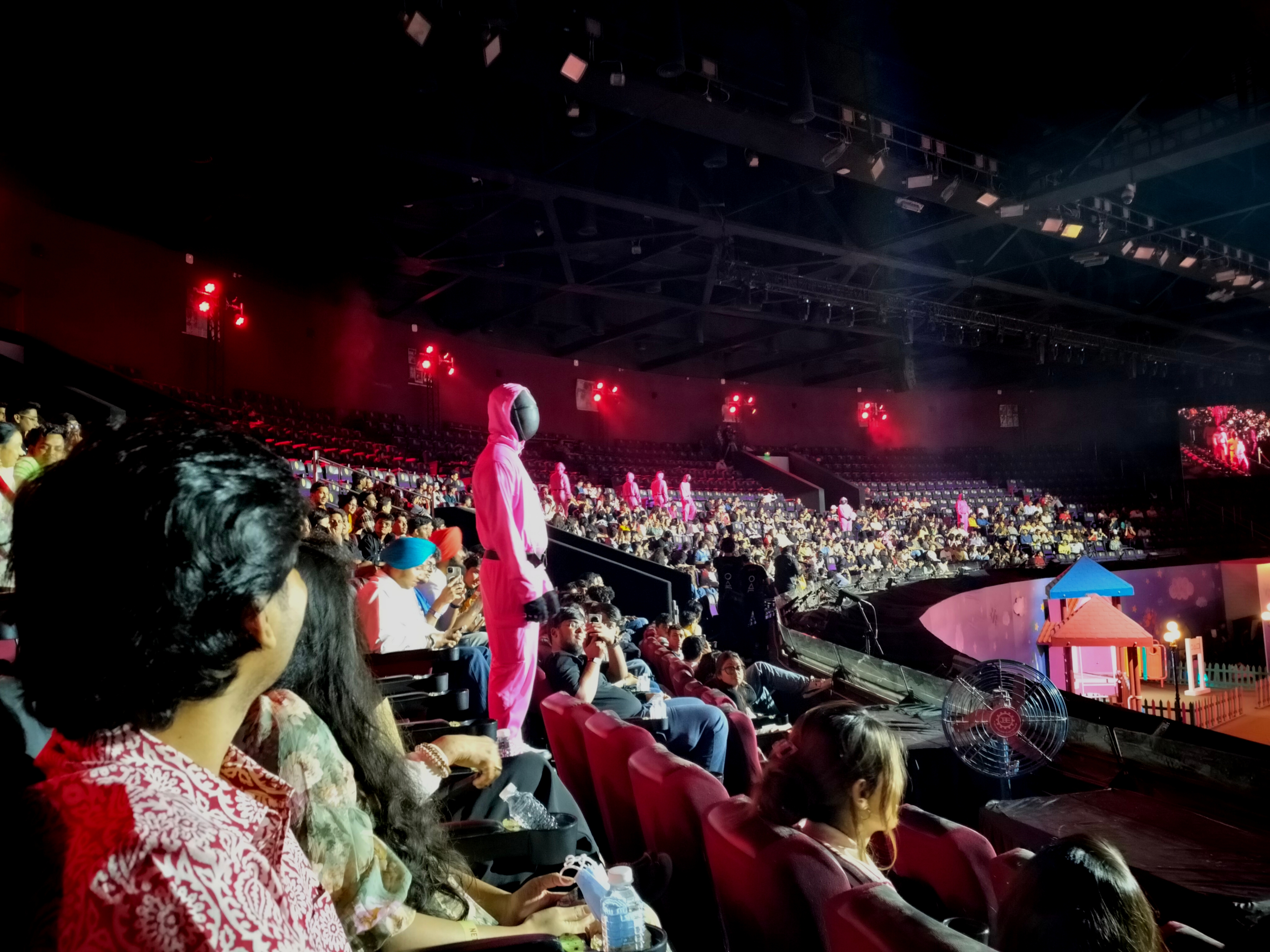 Audience watching an indoor event in a large arena, focused on a performer in a bright costume on stage