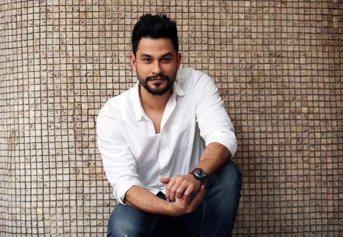 Person in a casual white shirt and jeans, sitting against a tiled wall, with a relaxed expression