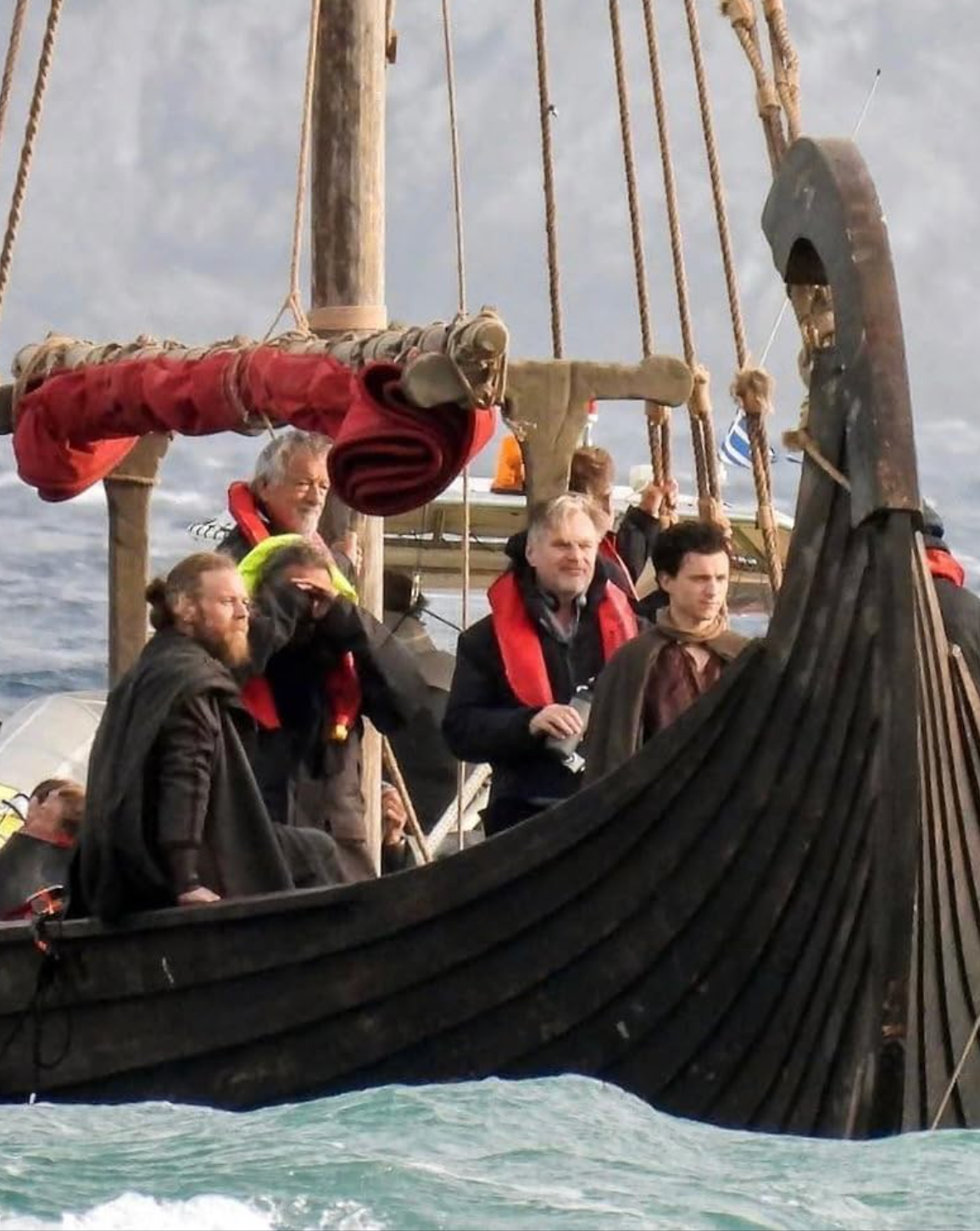 People wearing life vests on a Viking-style boat at sea, engaged in conversation