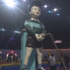 Statue of a child with a cap, striped shirt, and shorts holding a rope in an exhibition setting. People and displays visible in background