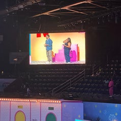 People on stage in front of a large screen at an event. A few people are seated in the audience