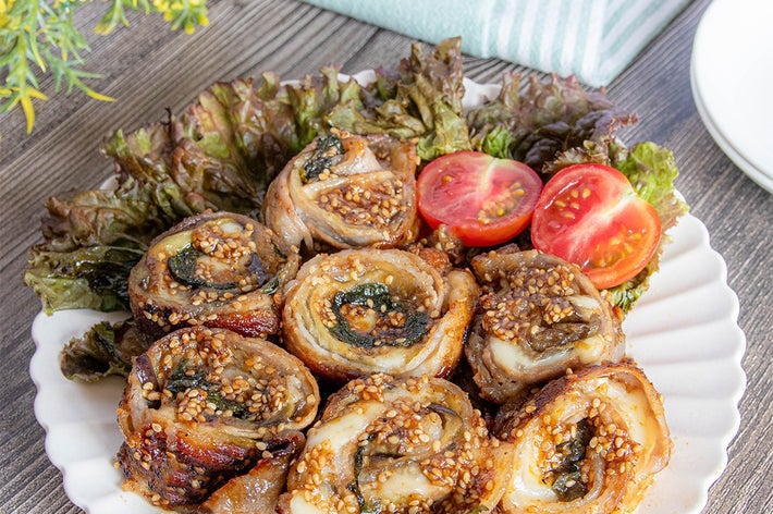おしゃれな白い皿に盛られた肉巻き料理。サラダ菜とミニトマトが添えられ、上品な盛り付けとなっている。
