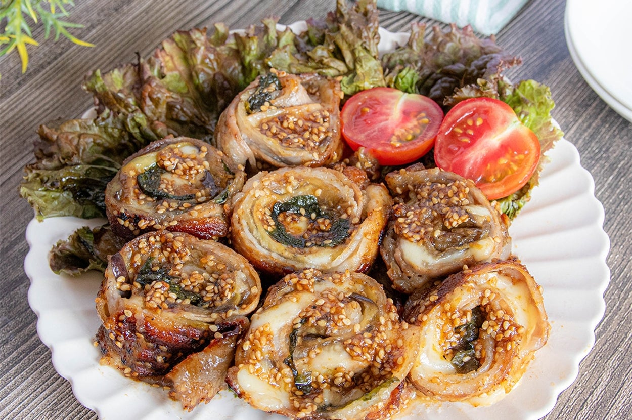おしゃれな白い皿に盛られた肉巻き料理。サラダ菜とミニトマトが添えられ、上品な盛り付けとなっている。