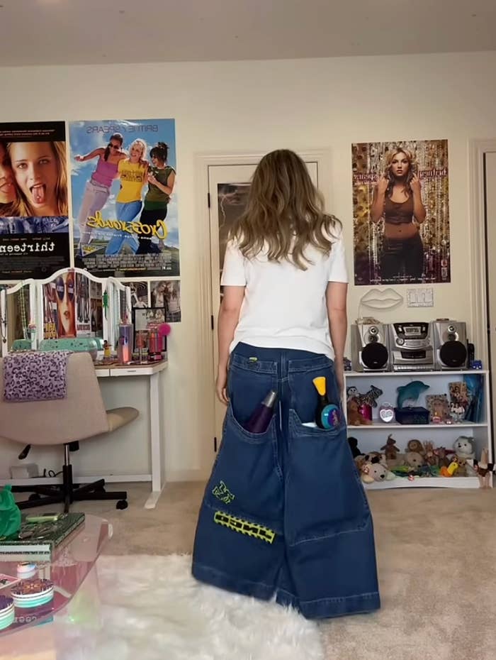 woman facing away, wearing excessively baggy jeans with monolithic pockets holding assorted ample objects