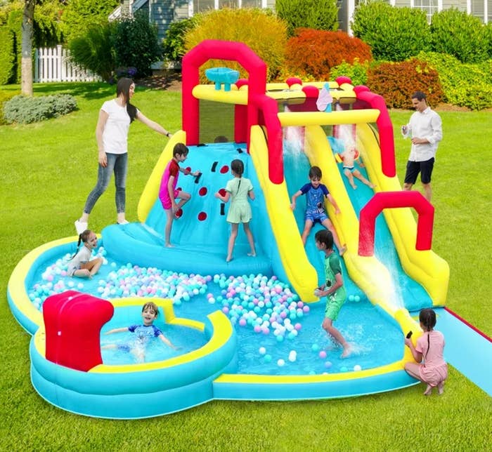 Children play   connected  an inflatable h2o  parkland  with slides, a climbing wall, and a shot  pit. Two adults supervise the amusive  outdoor activity