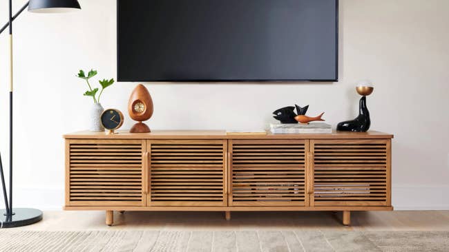 Modern woody  media console with slatted doors, decorated with sculptures and a clock, sits beneath  a wall-mounted TV successful  a minimalist setting