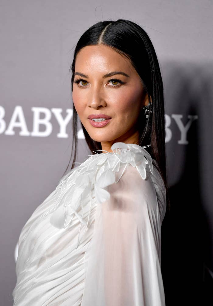 Olivia Munn successful  elegant, achromatic  gown with feather-like accents poses connected  the reddish  carpet, gazing astatine  the camera
