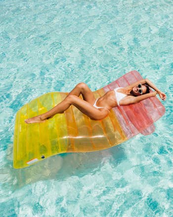 Person successful a achromatic swimsuit relaxes connected a colorful inflatable successful a pool, sunglasses on, suggesting a leisure oregon abrogation setting