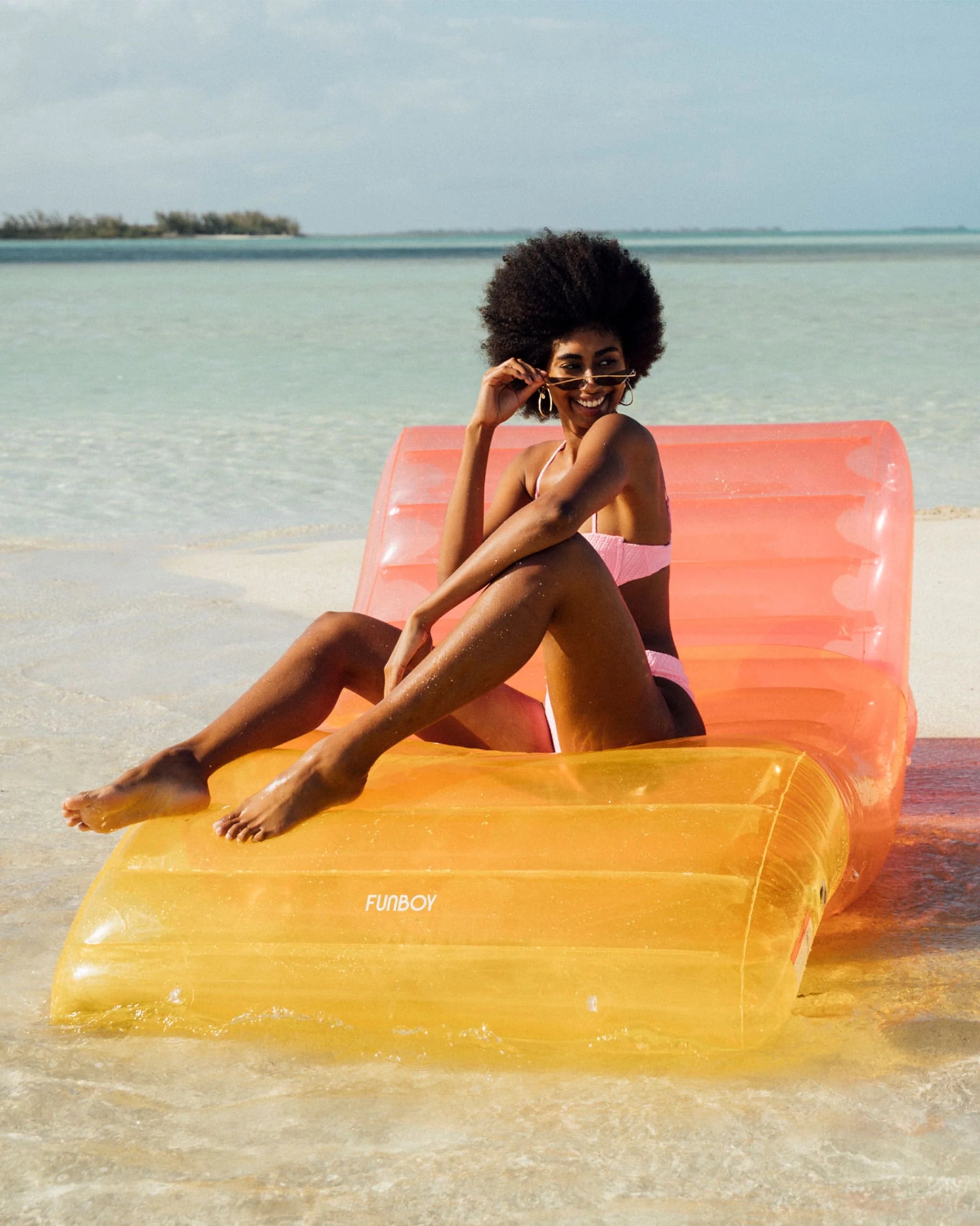 A idiosyncratic   lounges connected  an inflatable formation  seat  successful  shallow water, wearing sunglasses and a stylish swimsuit, with tropical scenery successful  the background