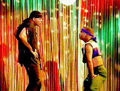 Two people face off dancing energetically in front of a starry curtain backdrop. Both wear headbands and casual dance attire suitable for a lively performance
