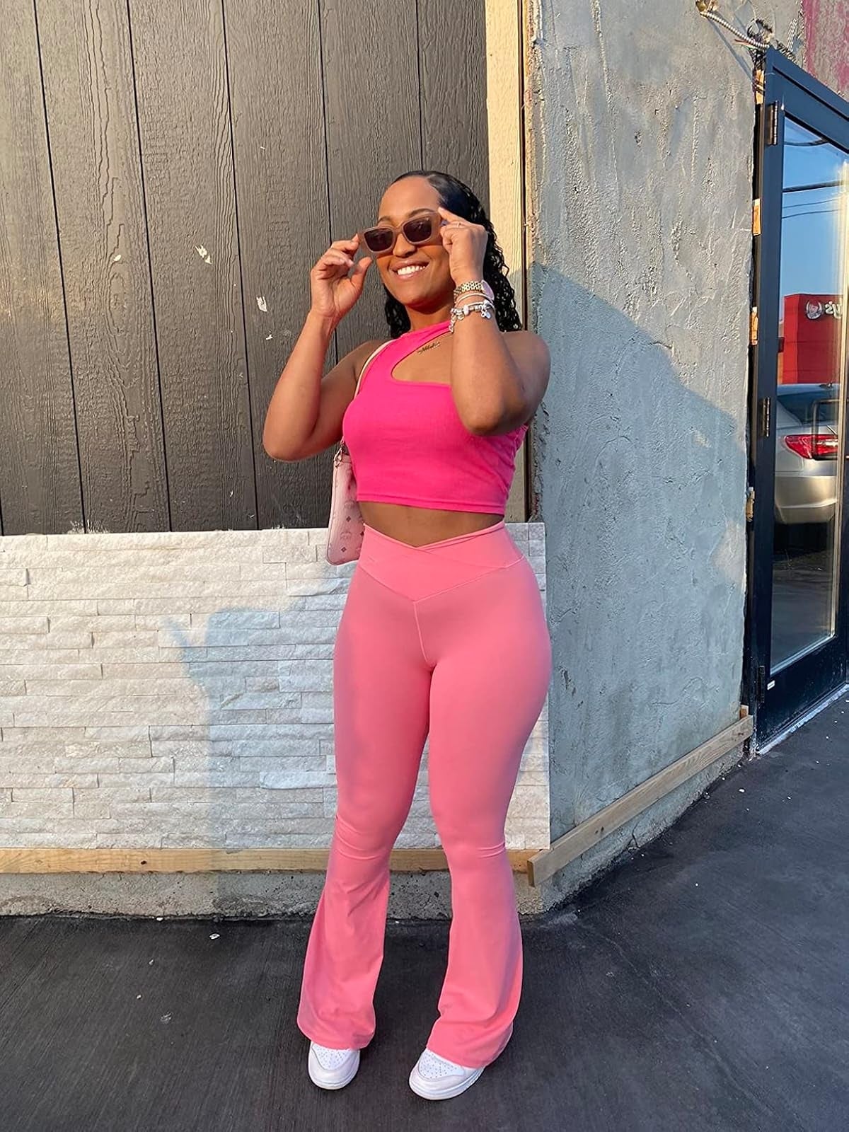 Person posing outdoors successful  stylish, fitted, sleeveless harvest  apical  and flared pants, with sunglasses and a crossbody bag, enjoying a casual moment