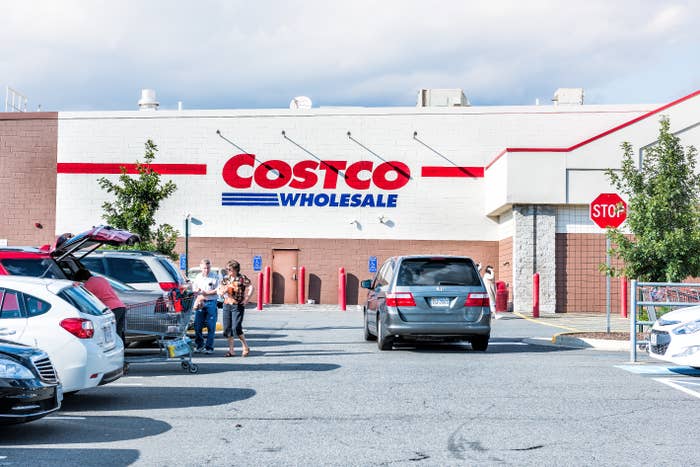 People load a car in a busy Costco parking lot with the store's sign in the background