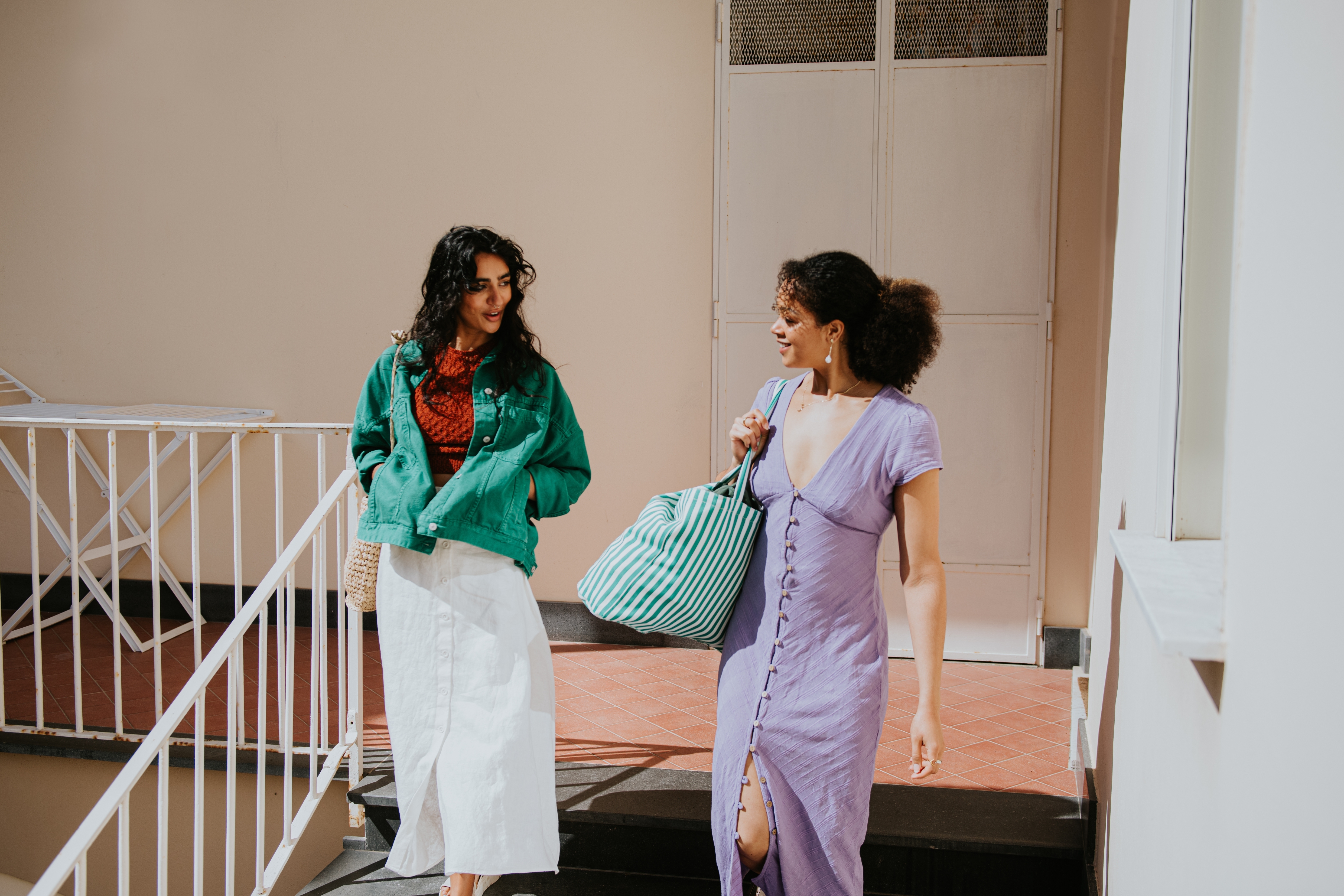 To kvinner vandrer sammen, den ene har på seg en uformell jakke og skjørt, og den andre i en knappet kjole, begge bærer poser og chatter