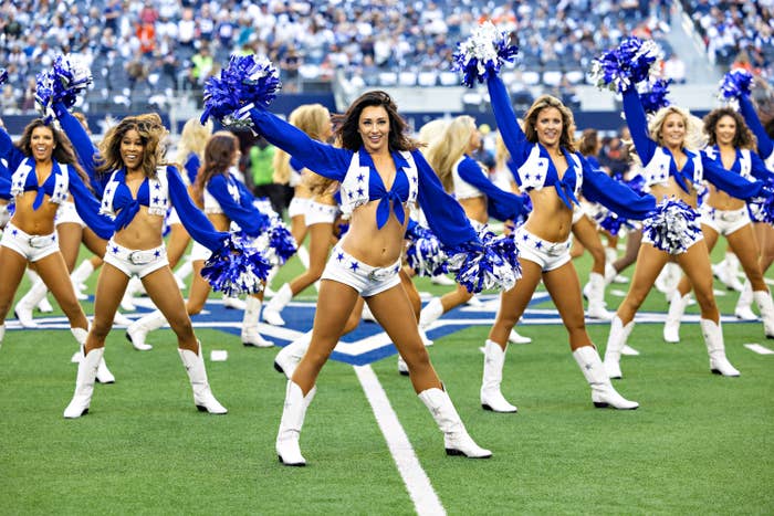 Cheerleaders in blue and white outfits perform energetically with pom-poms on a football field during a game