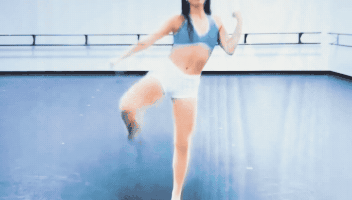 A dancer energetically performs a routine in a studio, wearing a sports top and shorts