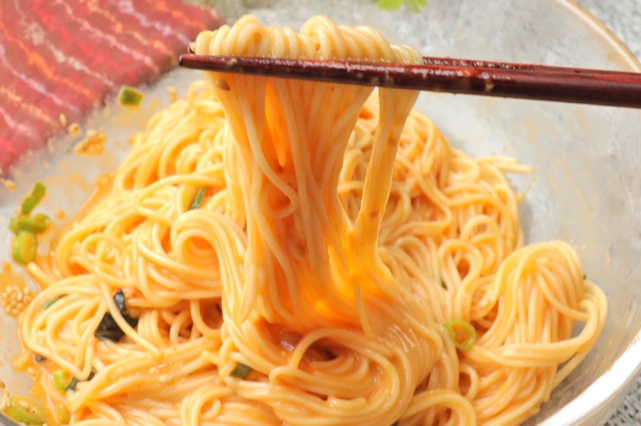 箸で持ち上げられたそうめんの盛り付け。植物の装飾が背景にあります。