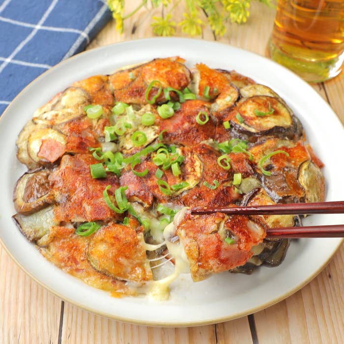 焼きナスとチーズがトッピングされた料理が皿に盛られている。箸が一切れ取っている。