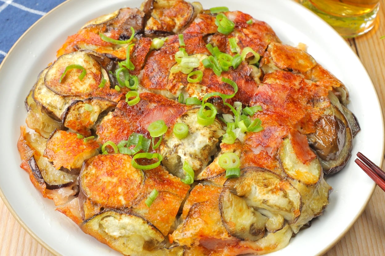 ナスとトマトを使った料理が皿に盛られている。料理の上には刻んだネギがトッピングされている。