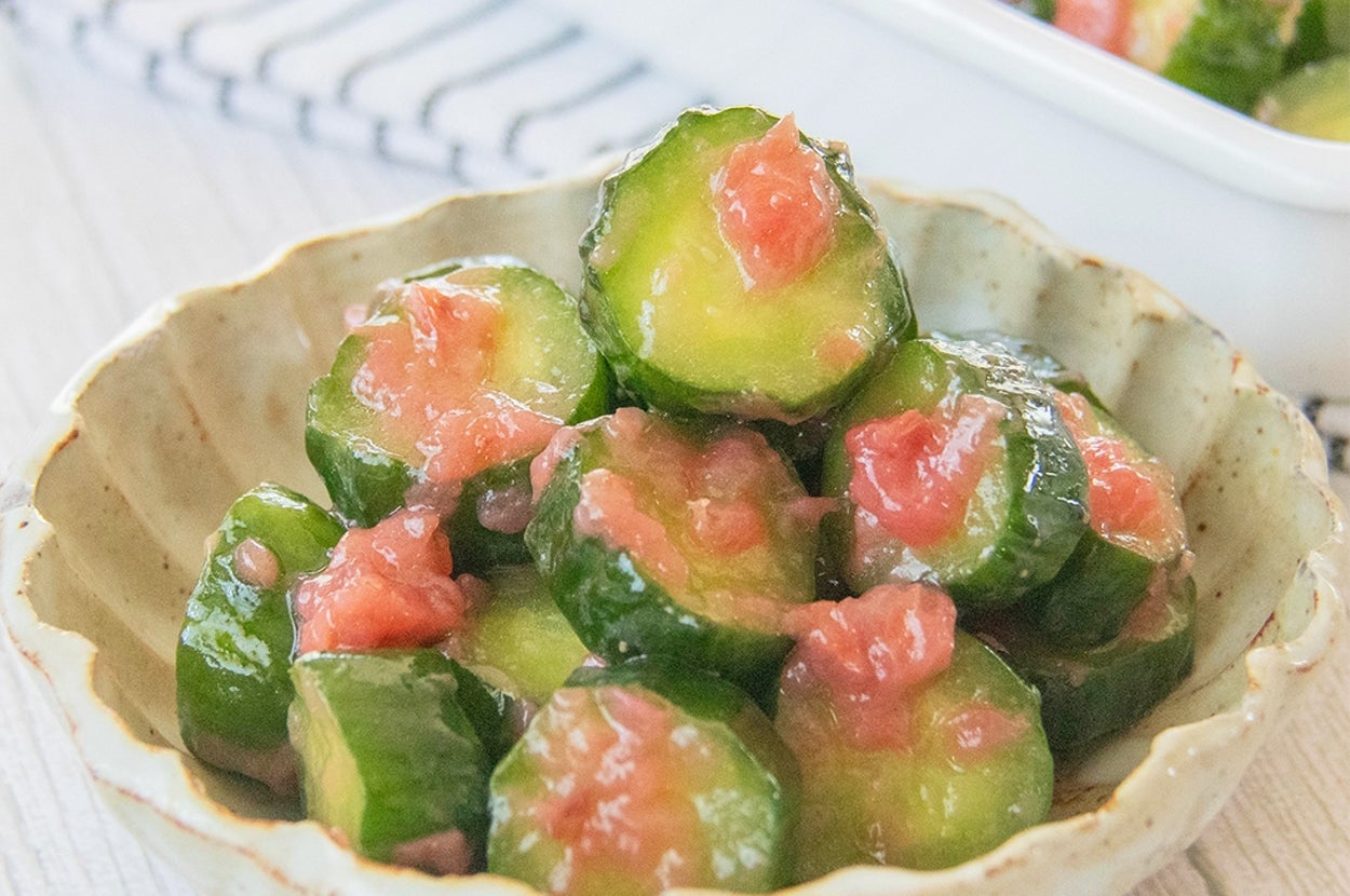 きゅうりと梅の和え物が小鉢に盛られている。背後に同様の料理が盛られた保存容器が見える。