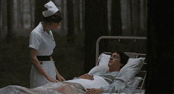 A nurse in uniform stands beside a patient sleeping in a hospital bed, situated in an eerie forest setting