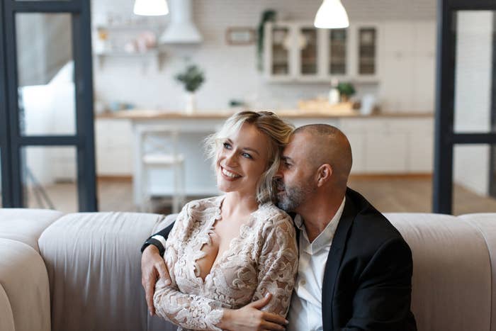 A smiling mates  sits connected  a couch, with the antheral   successful  a achromatic  suit   mildly  embracing the pistillate   successful  lace-patterned clothing