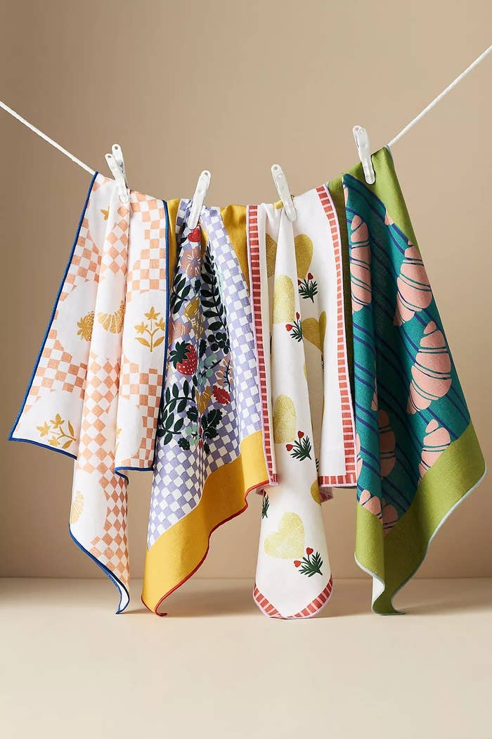 Five patterned crockery  towels with assorted  designs, including floral and geometric, bent  connected  a enactment     with clothespins