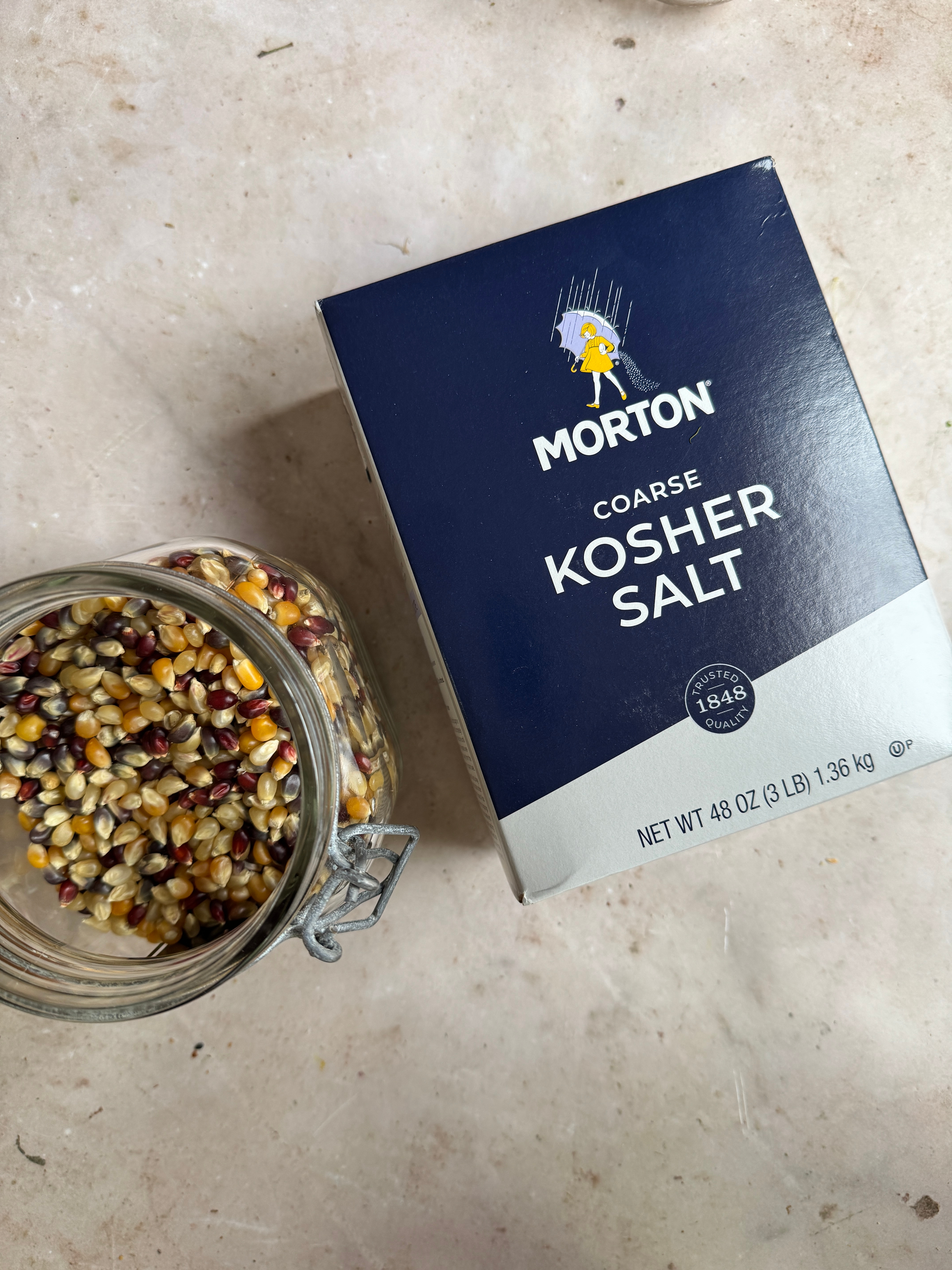 Box of Morton coarse kosher salt next to a jar of multicolored popcorn kernels on a countertop