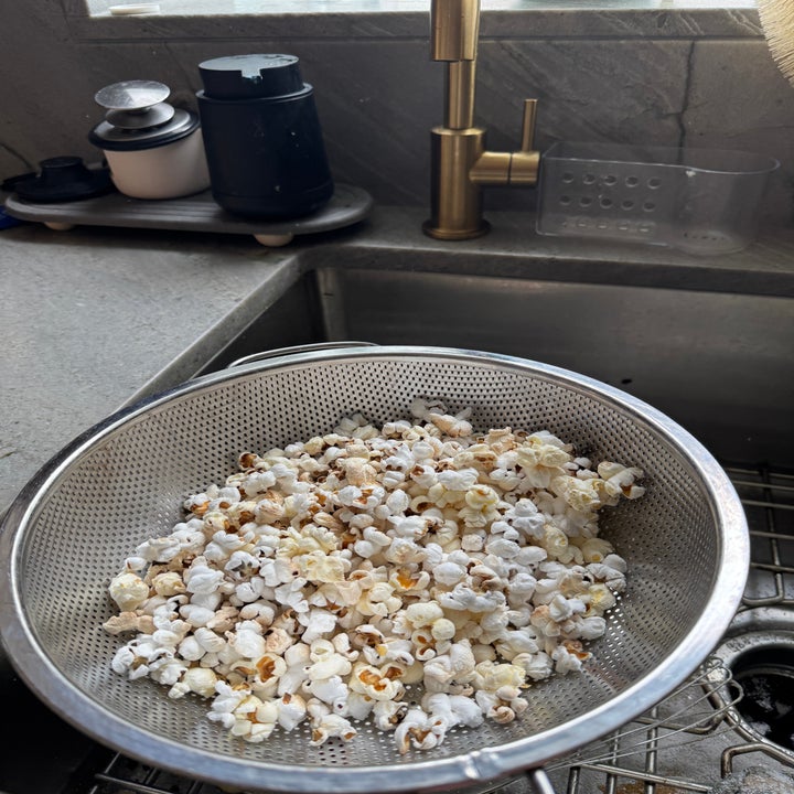 Popcorn in a metal strainer over a sink, with kitchen items in the background