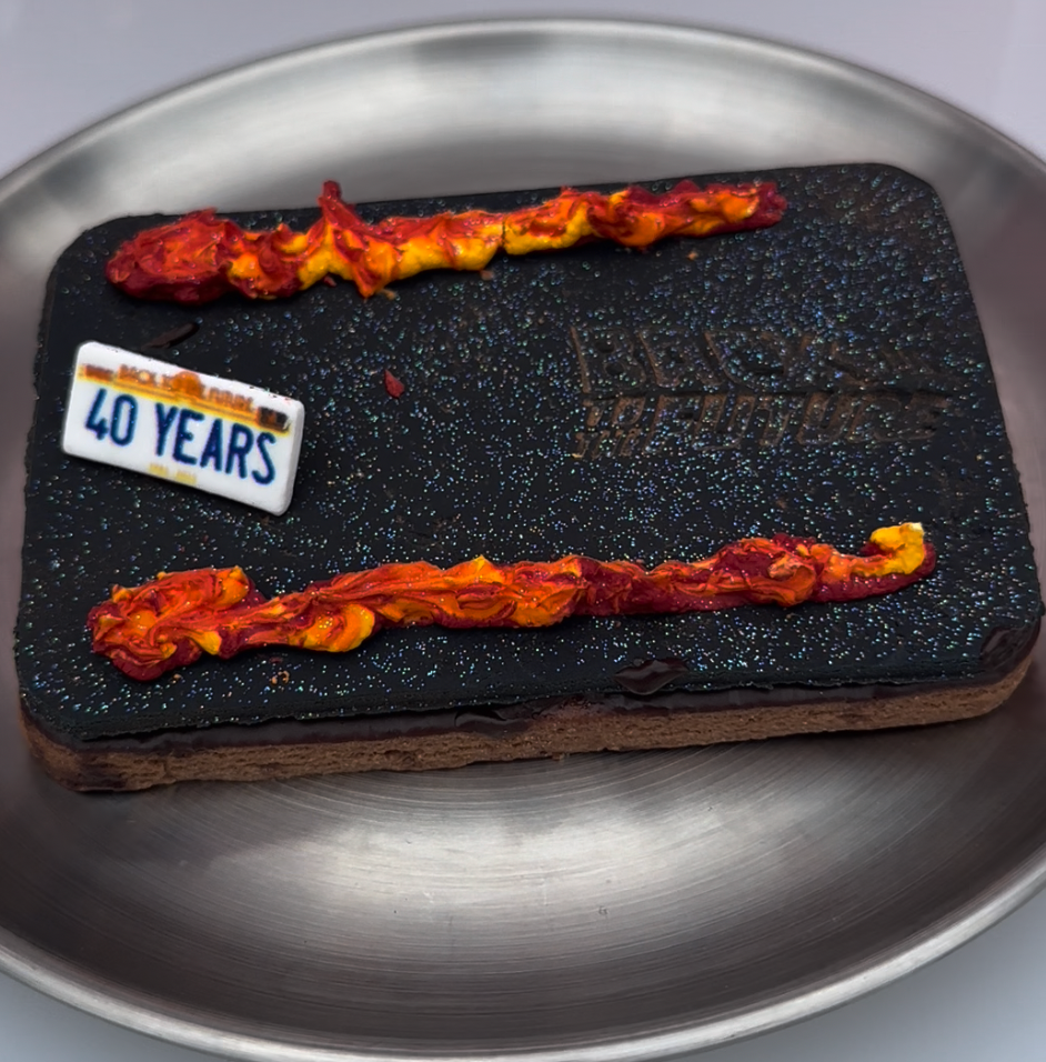 Rectangular cake with two red and yellow icing lines, a &quot;40 Years&quot; plaque, and an embossed design on a round metal plate