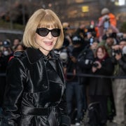 Person in fashionable black coat and sunglasses poses outdoors as photographers capture the moment