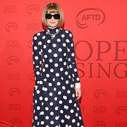 Person in polka dot dress and sunglasses poses on a red carpet event backdrop with "Hope Rising" text