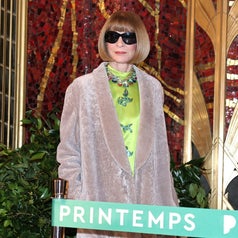 Person in stylish coat and sunglasses stands by a "Printemps" sign, with a vibrant patterned top underneath