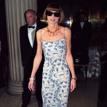 Person in a patterned evening gown, bold necklace, and sunglasses at a formal event, standing confidently
