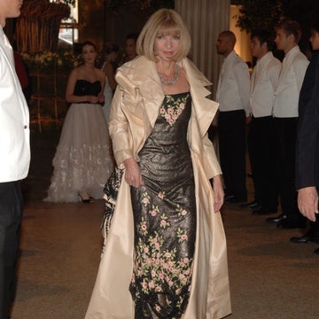 Woman in elegant floral gown with a satin robe walks past people in formal attire at a glamorous event