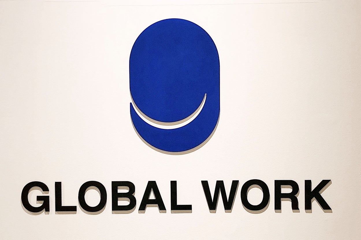 白い壁に青い円形ロゴと「GLOBAL WORK」の黒い文字が大きく描かれています。ロゴはシンプルでモダンなデザインです。