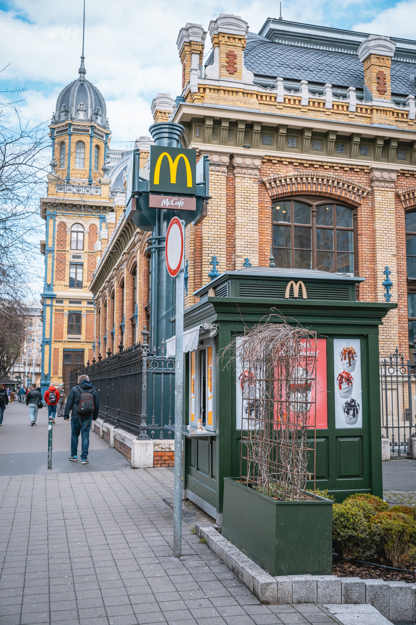 Historic European building with McDonald's signage in the foreground, pedestrians walking nearby on a city street